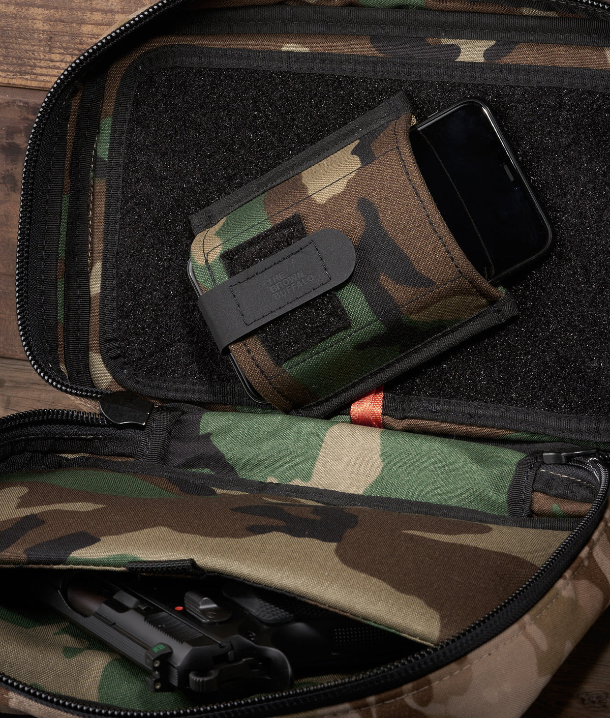 Muzzle Mask camo wallet with The Brown Buffalo logo in a tactical bag beside a smartphone on Tampa Home & Garden Store