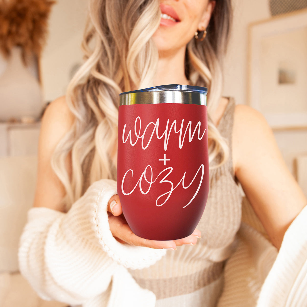 Warm + Cozy red 17oz tumbler with white script and metal lid held by a smiling woman on Tampa Home & Garden Store