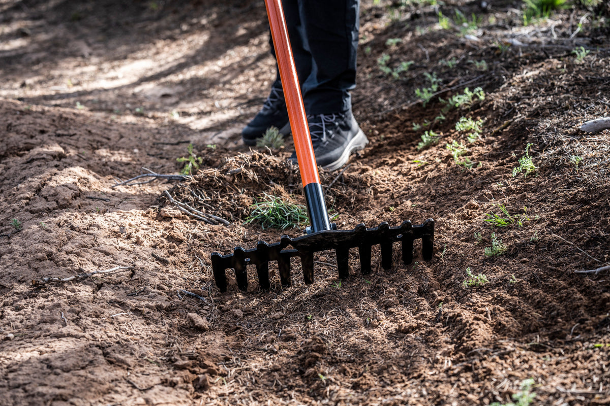 Weston rake by Backslope Tools with orange handle and black tined head in dirt on Tampa Home & Garden Store
