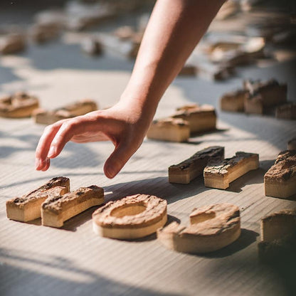 Wooden alphabet letter natural wood finish, hand reaching toward scattered blocks on a light surface on Tampa Home & Garden Store